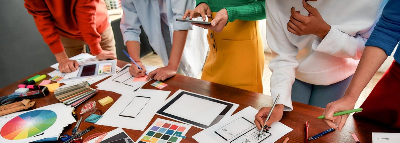 Custom Web Design wide image with people standing around a desk pointing at papers