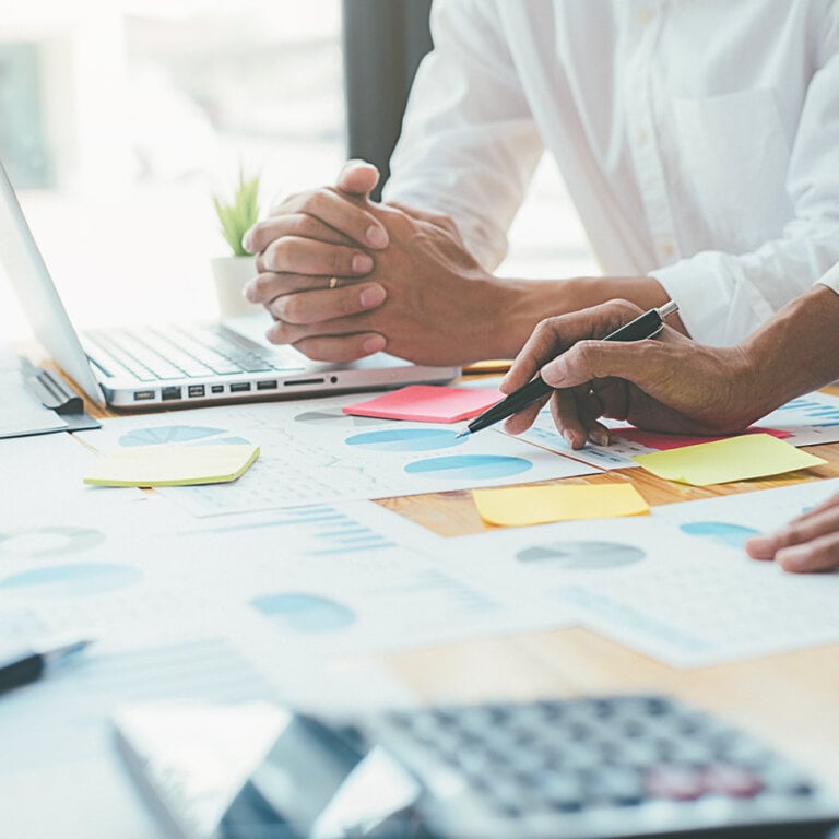 Person planning web strategy with charts, sticky notes, and a laptop
