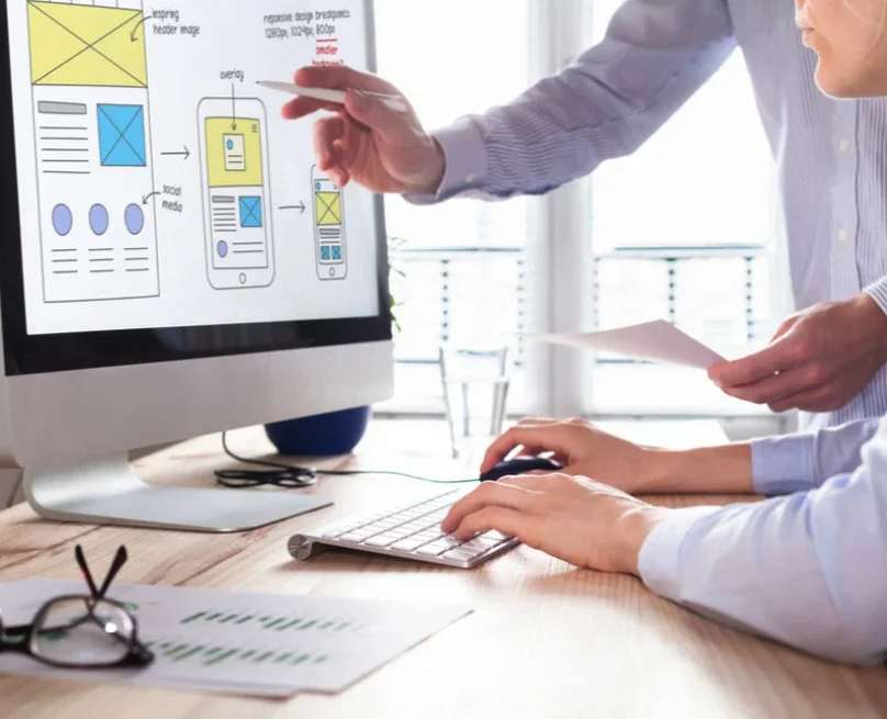 Two people reviewing responsive website wireframes on a monitor