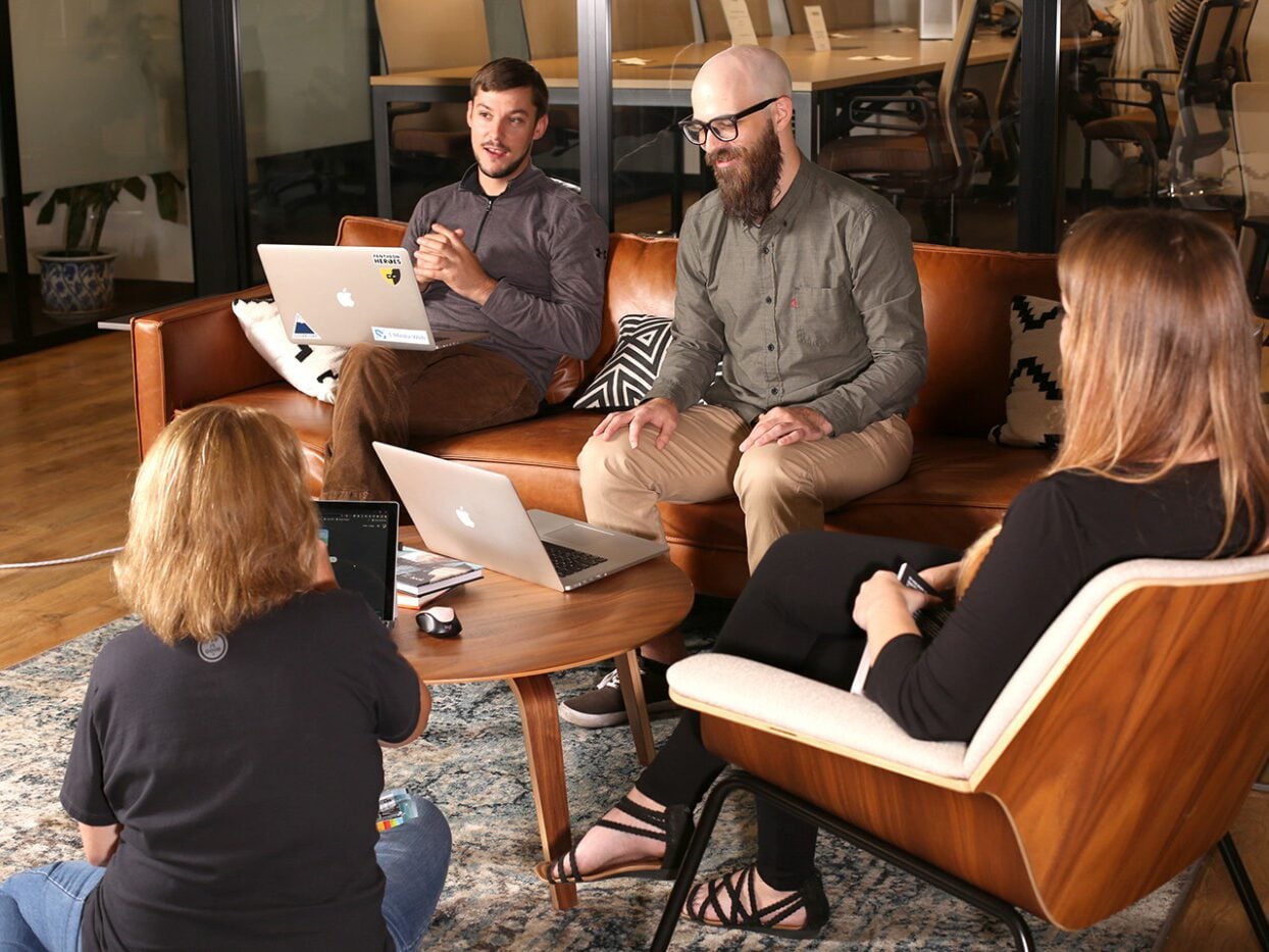 Four colleagues collaborating over laptops in a casual office lounge