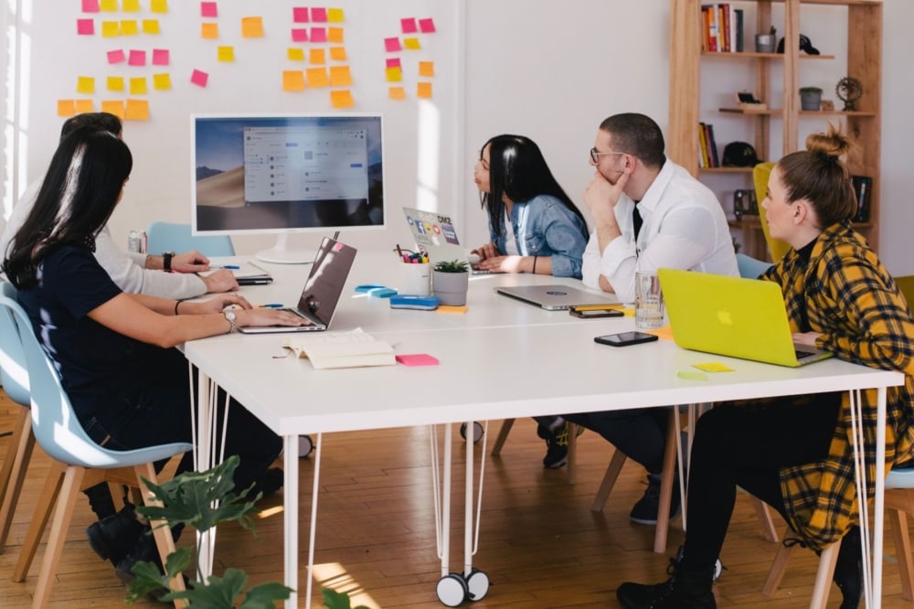 A group of coworkers at table during a meeting looking at a tv monitor