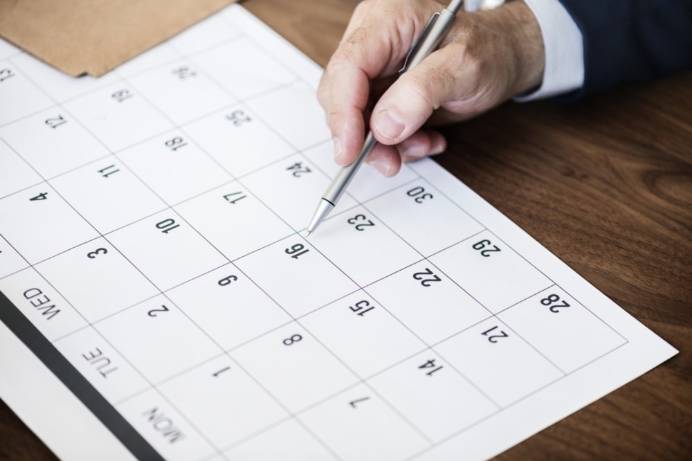 desktop calendar with man writing on one of the dates with an ink pen